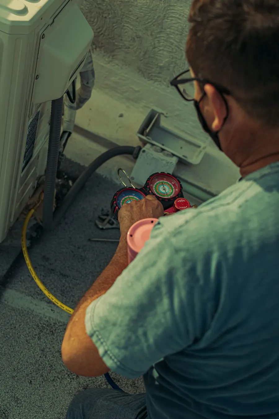Technician reading manifold gauges while servicing an air conditioning unit
