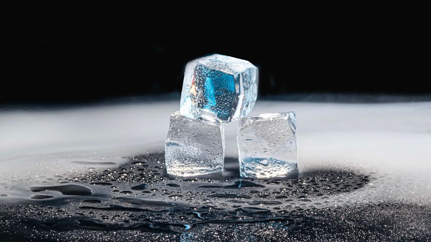 Crystal clear ice cubes resting on a dark, wet surface